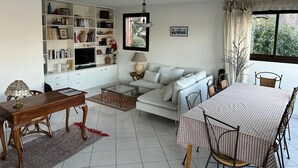 Un salon avec un canapé, une table basse et une table à manger. On y trouve également une bibliothèque et un téléviseur.