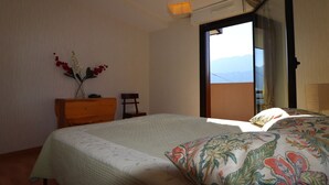 Une chambre à coucher comprenant un lit, une commode, une chaise et une fenêtre donnant sur les montagnes.