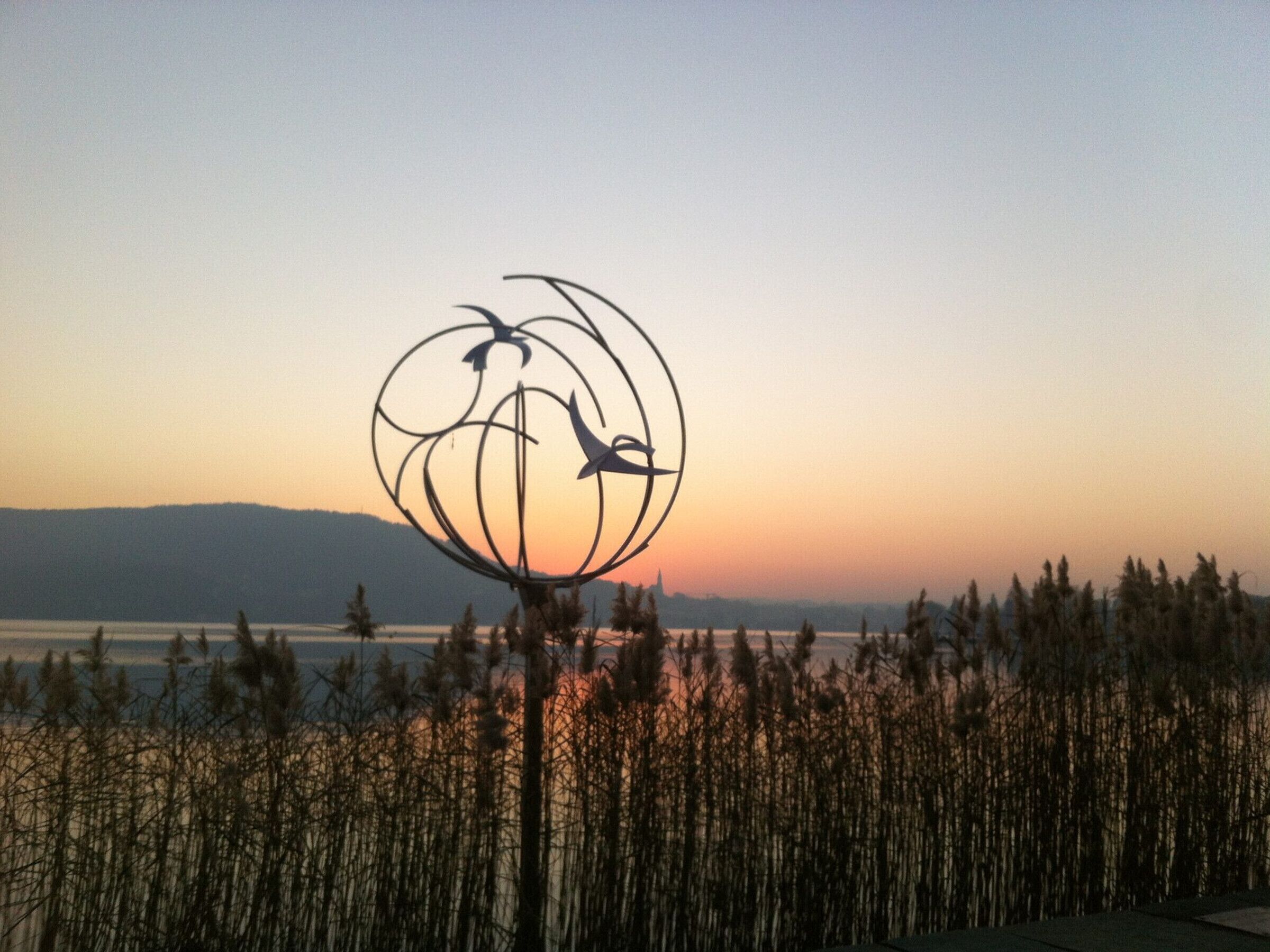 A sculpture of birds on a globe, surrounded by tall grasses, with a sunset in the background.