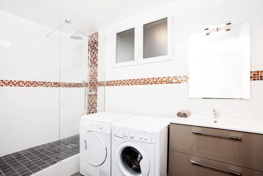 Un bany modern amb una cabina de dutxa de vidre, una rentadora i un moble de bany amb mirall.