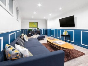 A modern living room with a blue and white color scheme, a sectional sofa, a coffee table, and a flat-screen TV mounted on the wall.