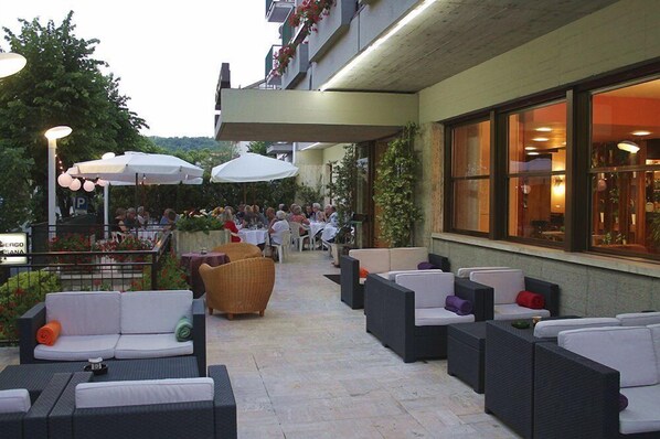 Un patio al aire libre con mobiliario de mimbre, sombrillas y mesas.