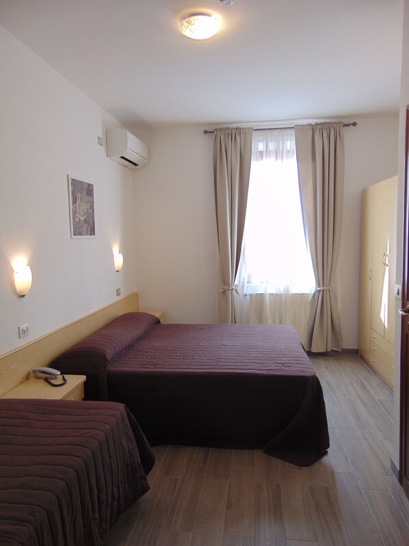 Habitación de hotel con dos camas, una mesita de noche con teléfono, aire acondicionado de pared y una ventana con cortinas.