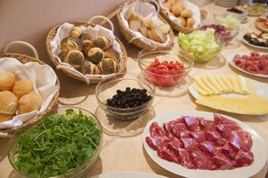 Una mesa con diversos alimentos como pan, queso, carnes y verduras.