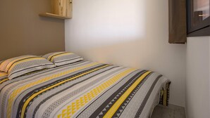 Ein Bett mit einem gemusterten Überwurf, einem Holzregal und einem Fenster mit Vorhang.