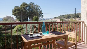Ein Holztisch mit einer Solarleining, einer blauen Flasche und einer Tasse auf einem Balkon mit roter Brüstung.
