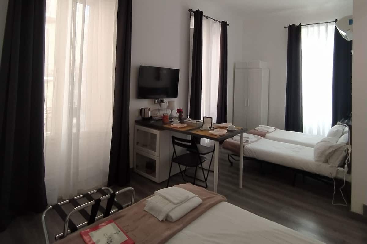 A hotel room with a bed, a desk with a computer, a TV, and a small kitchenette.