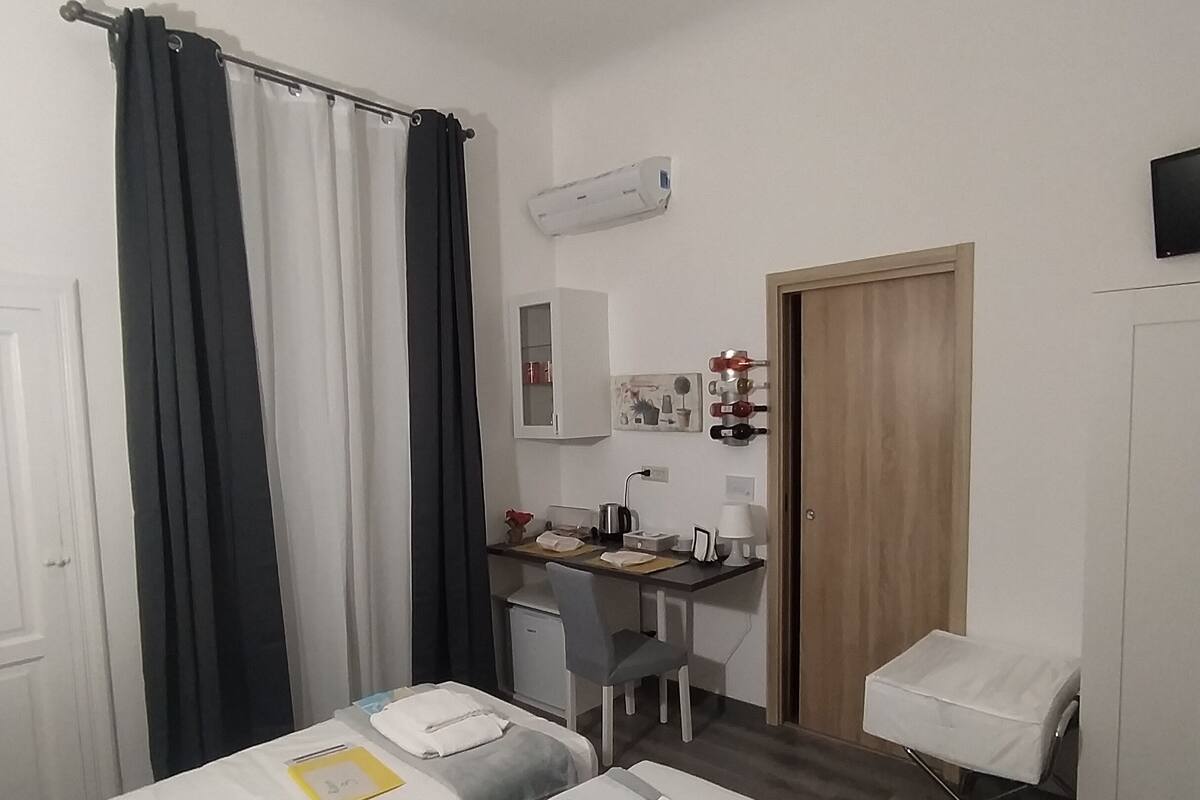 A hotel room with two beds, a desk, a chair, a wardrobe, and an air conditioning unit.