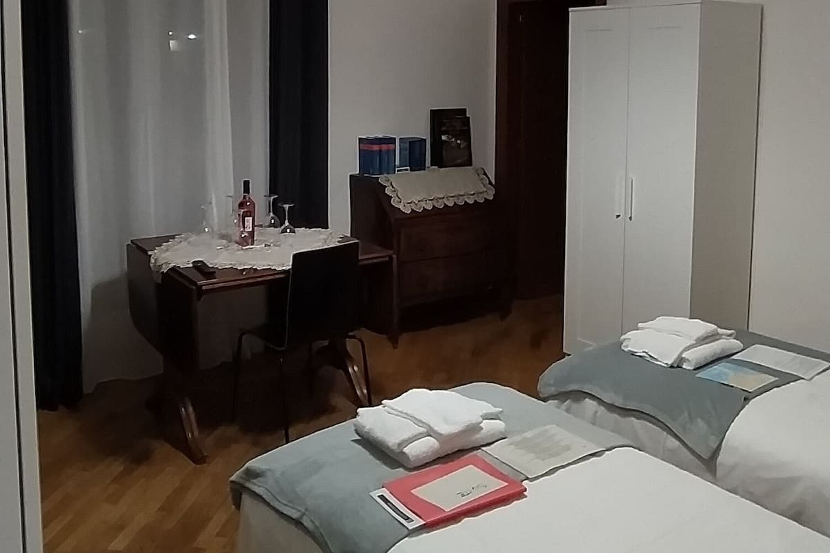A hotel room with two beds, a desk with a chair, a wardrobe, and a hanging light fixture.