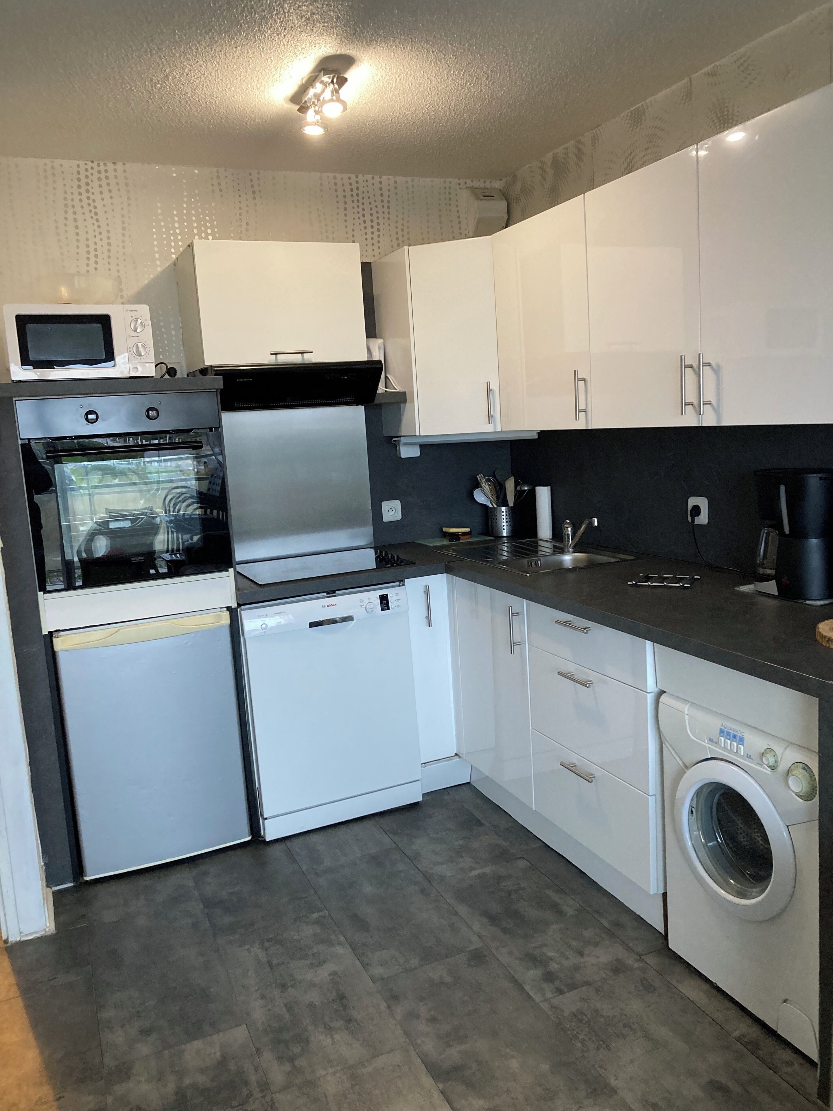 Una cucina moderna con mobili bianchi, forno integrato, microonde, lavastoviglie e lavatrice.