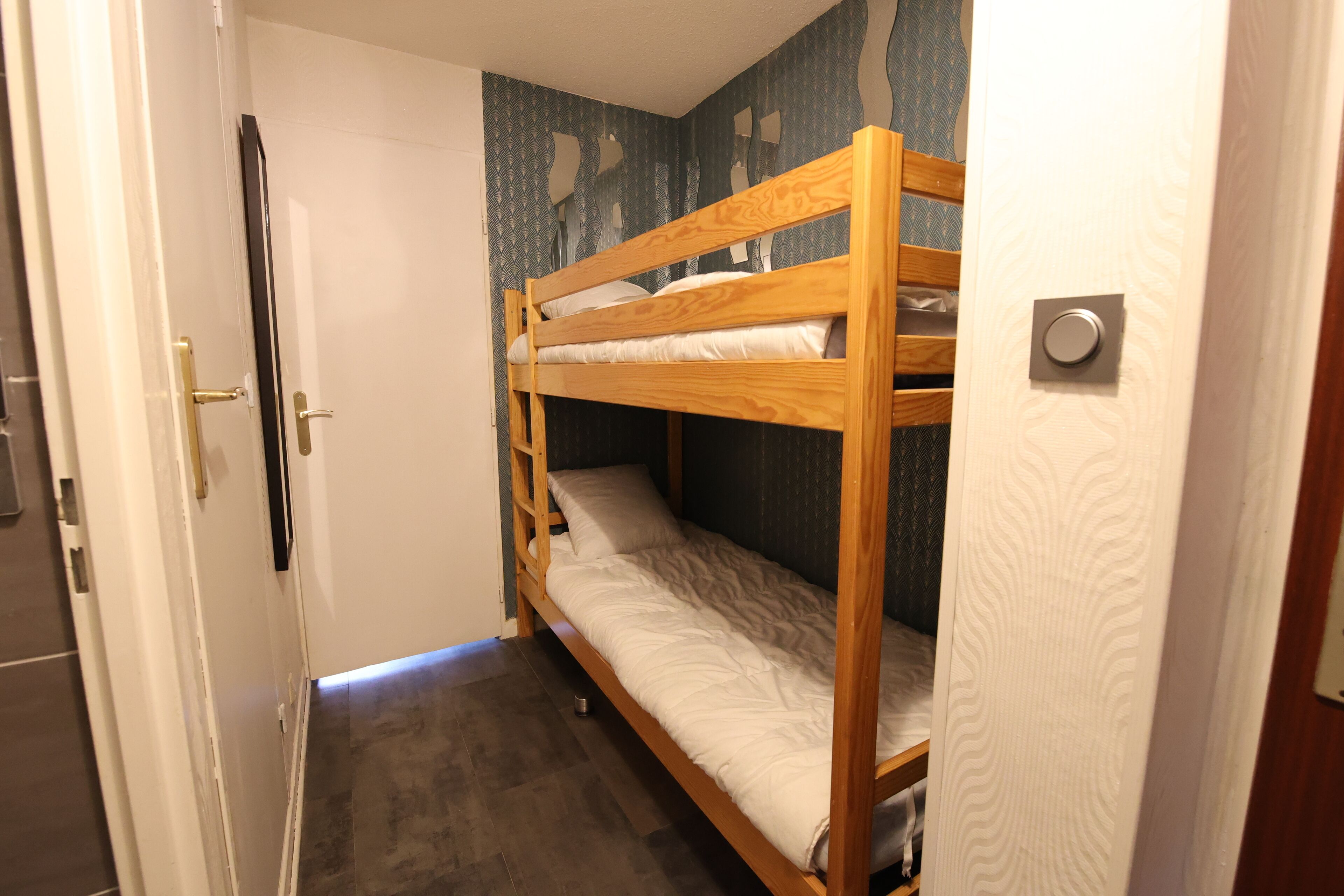 A bunk bed in a room with a door, a patterned wall, and a tiled floor.
