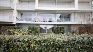 Un edificio de varios pisos con balcones, ventanas amplias y un seto bien cuidado en primer plano.