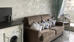 Una sala de estar con sofá, lavadora y comedor con una silla.