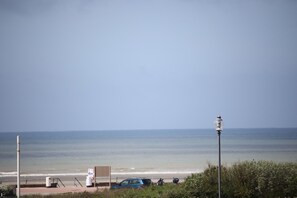 Une vue sur la plage, avec un ciel dégagé, un lampadaire et une voiture bleue garée près de l’eau.