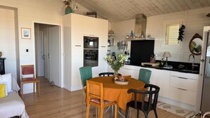 A modern kitchen with white cabinets, a dining table with chairs, and a wooden floor. - Authentic chalet on stilts facing the sea (15 m) - 4-star services (gruissan)