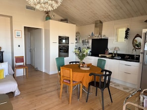 A modern kitchen with white cabinets, a dining table with chairs, and a wooden floor. - Authentic chalet on stilts facing the sea (15 m) - 4-star services (gruissan)