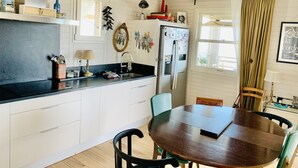 A kitchen with a wooden ceiling, a dining table with chairs, a refrigerator, and various kitchen utensils on the wall. - Authentic chalet on stilts facing the sea (15 m) - 4-star services (gruissan)