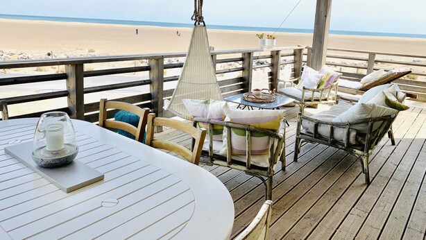 A wooden deck with a table and chairs overlooking a beach. - Authentic chalet on stilts facing the sea (15 m) - 4-star services (gruissan)