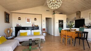 A spacious living area with a wooden ceiling, a dining table with chairs, a sofa, and a television. - Authentic chalet on stilts facing the sea (15 m) - 4-star services (gruissan)