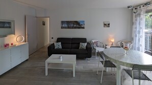 A modern living room with a black sofa, white coffee table, and a dining area with a round table and chairs. - Central Arcachon - Charming 2-BR for 4 with Balconies & Parking (Arcachon)