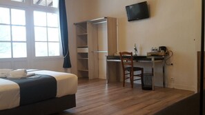 Une chambre d’hôtel comprenant un lit, un bureau avec une chaise, un téléviseur fixé au mur et une fenêtre avec des rideaux.