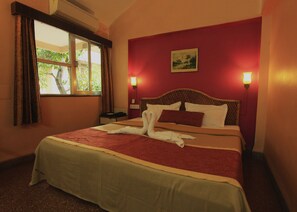 Habitación de hotel con cama, mesita de noche, ventana con cortinas y un cuadro en la pared.
