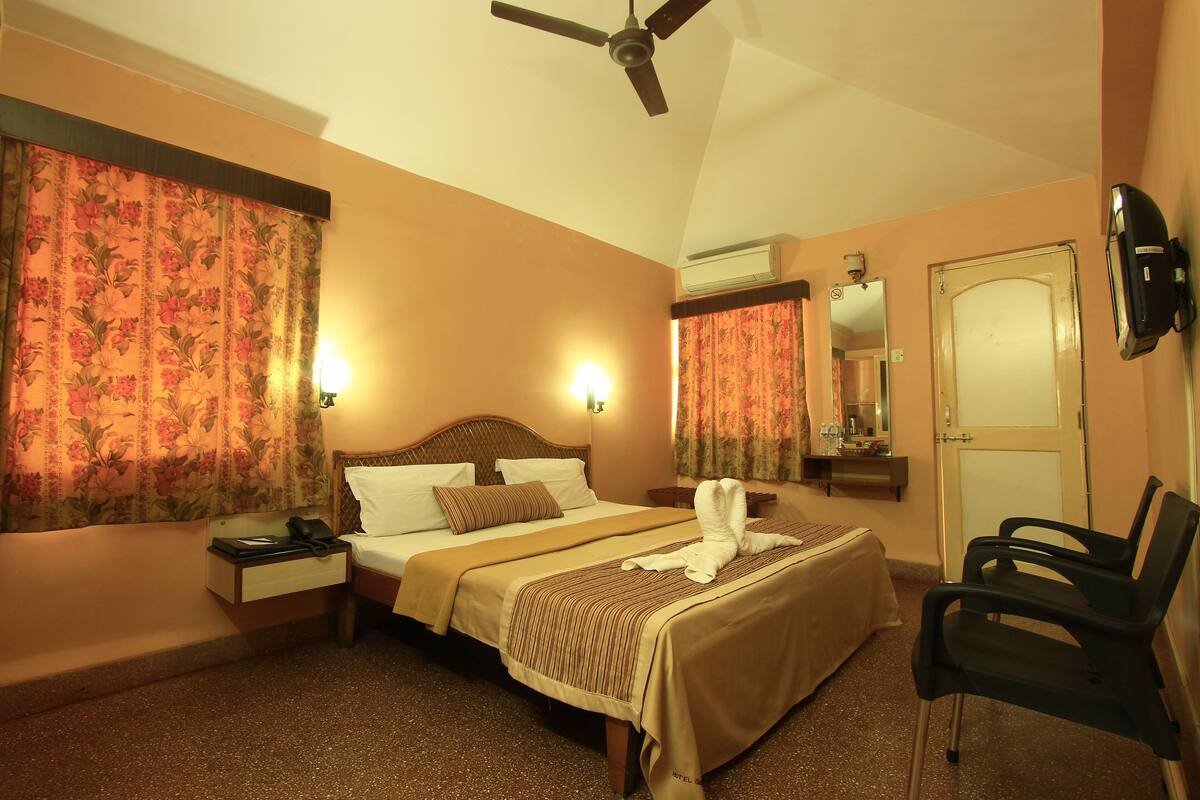 A hotel room with a bed, bedside table, chair, ceiling fan, and a mirror.