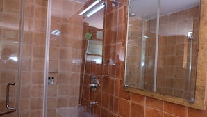 A bathroom with a glass shower enclosure, a wooden vanity, and a large mirror. - Hotel Gopika International (Panaji)