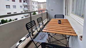 A balcony with a table and chairs, a window, and a view of neighboring buildings. - Annecy: Spacious F2 50m from lake with balcony and parking (Annecy)