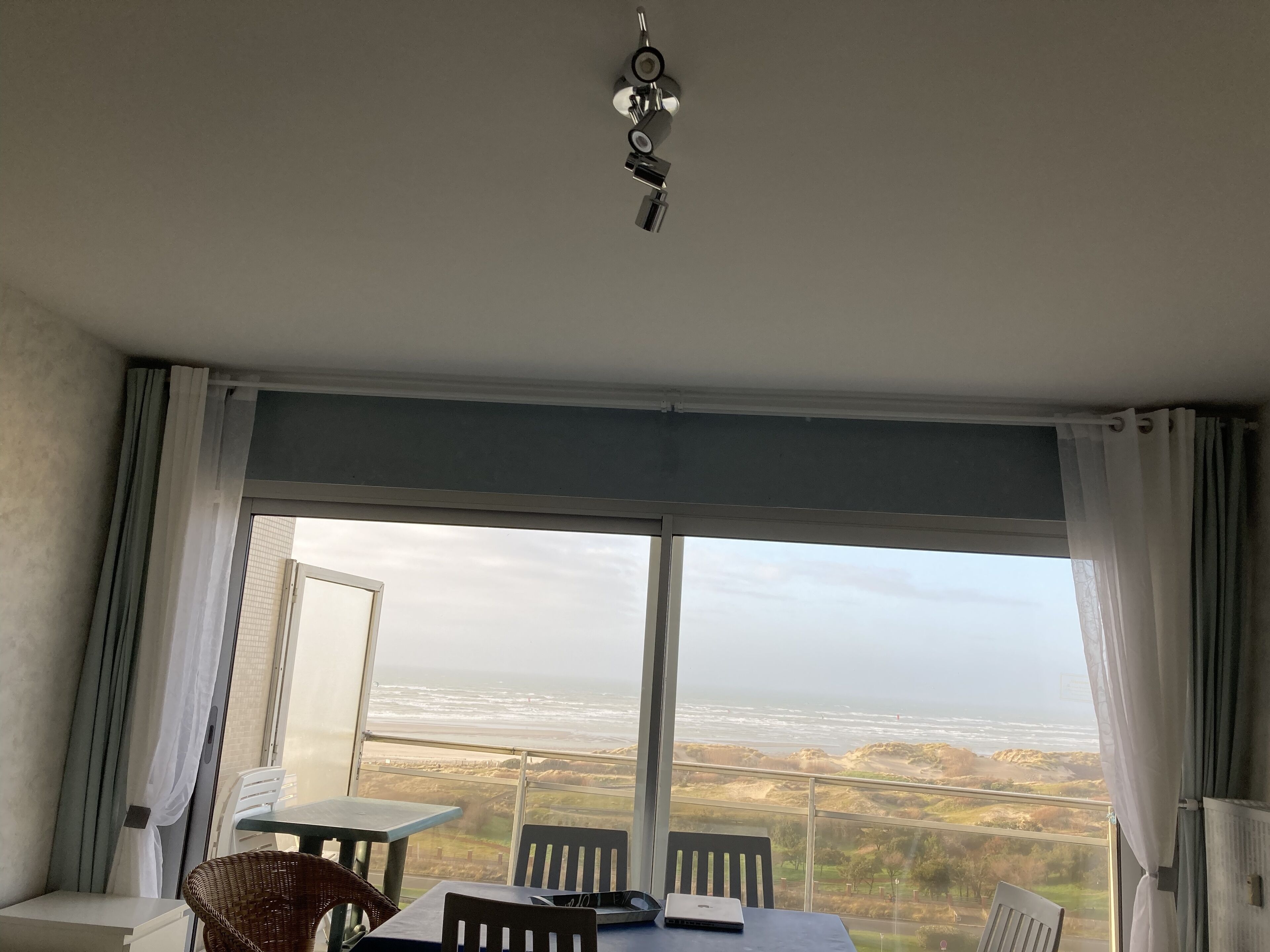 Une pièce dotée d’une grande fenêtre donnant sur un paysage côtier, d’une table avec des chaises et d’un luminaire suspendu.