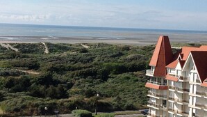 Ein mehrstöckiges Hotel mit rotem Dach, umgeben von üppiger Vegetation und einem Strand im Hintergrund.