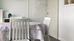 Ein Zimmer mit zwei weißen Stühlen, einem Tisch, einem an der Wand befestigten Flachbildfernseher, einer Stehlampe und einem Fenster mit Vorhängen.