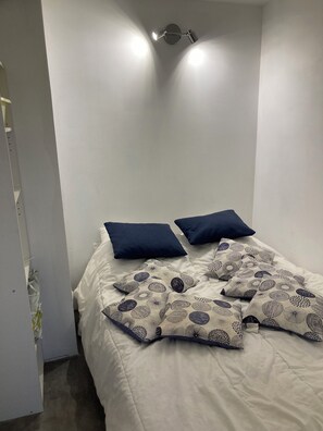 Une chambre à coucher avec un lit, deux oreillers, une couverture à motifs et un luminaire fixé au mur.