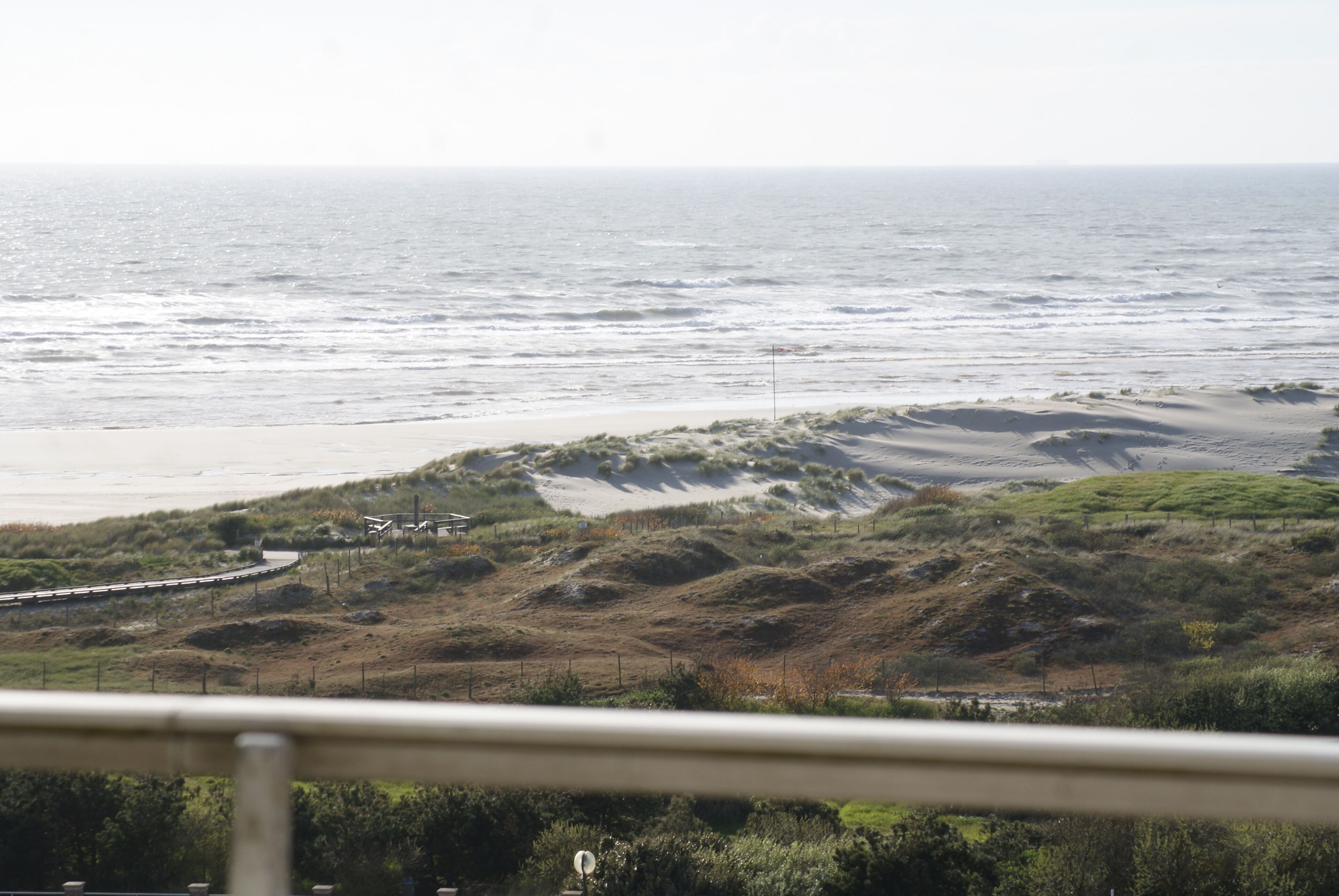 Eine Küstenlandschaft mit Sandstrand, grasbewachsenen Dünen und einer sich an der Küste entlangziehenden Straße.