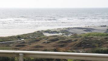 Eine Küstenlandschaft mit Sandstrand, grasbewachsenen Dünen und einer sich an der Küste entlangziehenden Straße.