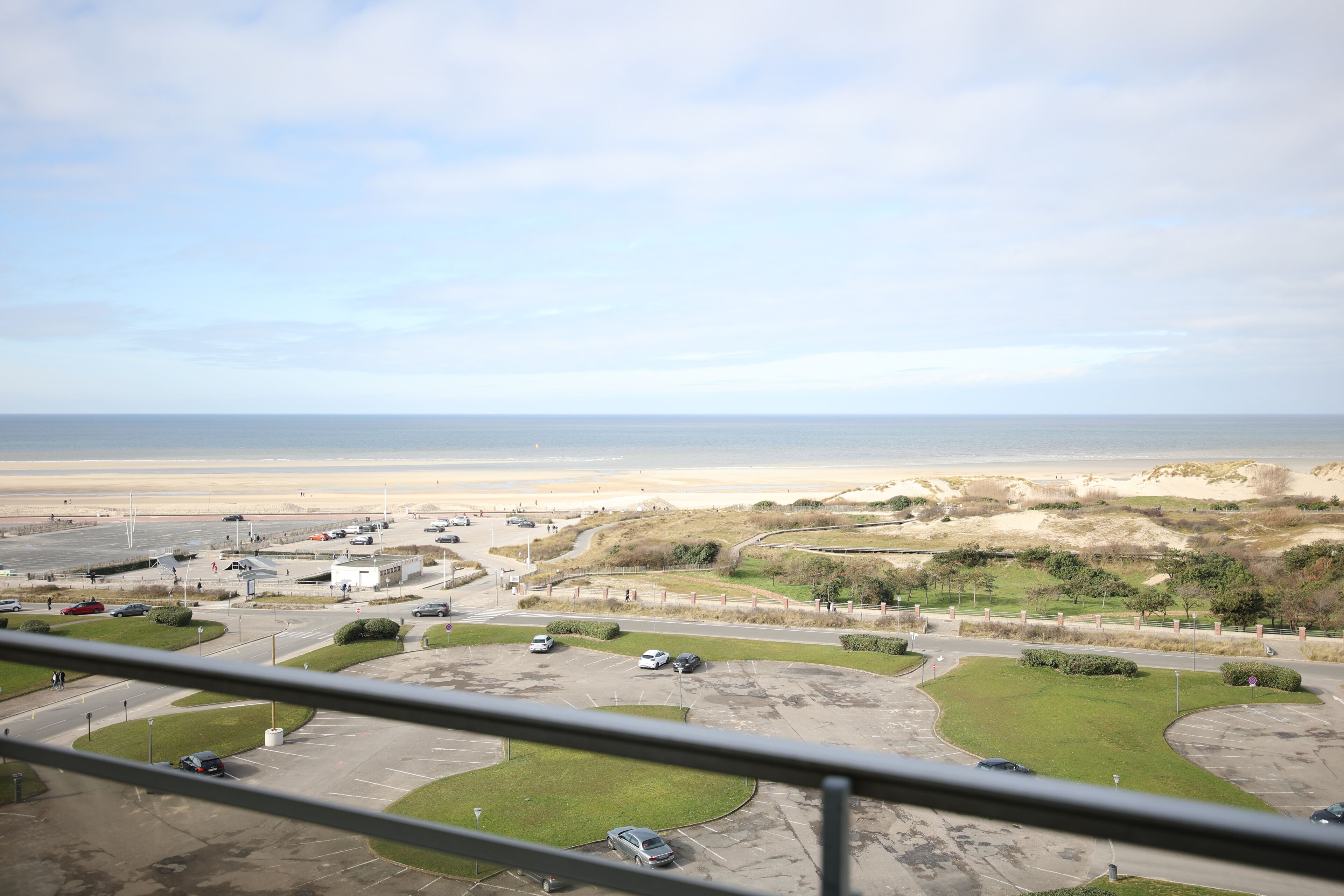 Blick auf die Küste mit einem Parkplatz, Gebäuden und einem Strand im Hintergrund.
