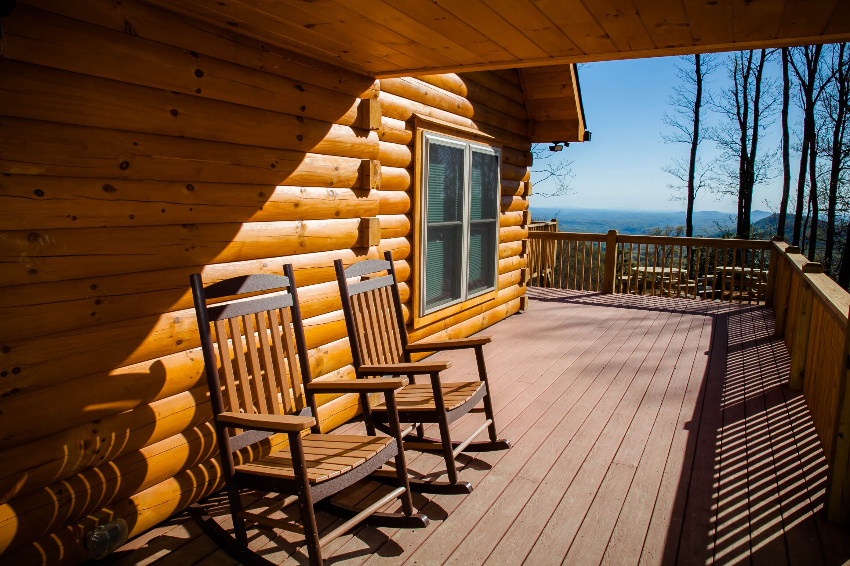 A wooden cabin with a deck featuring rocking chairs and a view of the landscape.