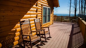 Eine Holzdiele mit einer Terrasse, auf der Schaukelstühle stehen und die Landschaft überblickt.