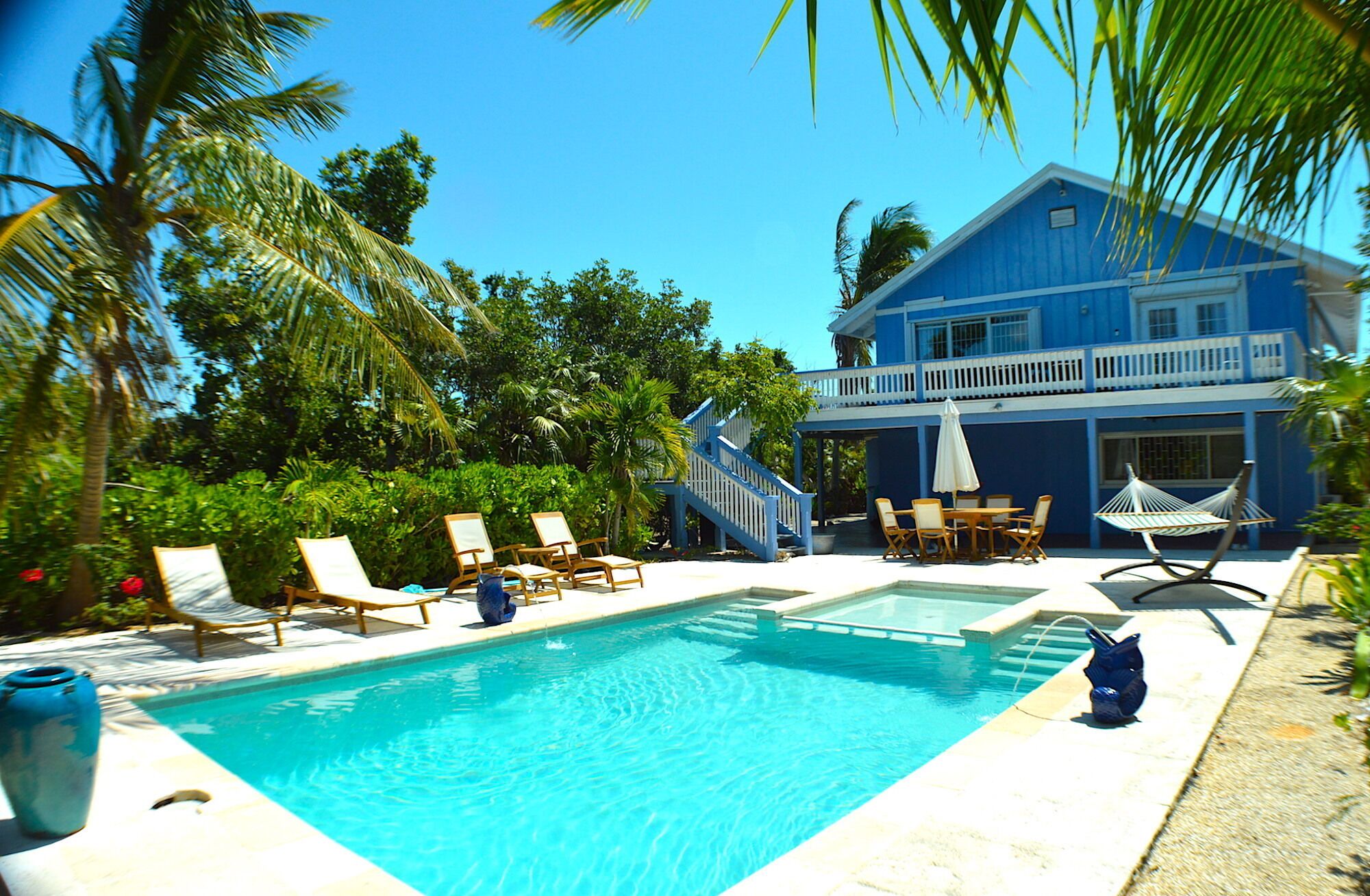 A pool area with lounge chairs, a dining set, and a two-story building with a balcony.