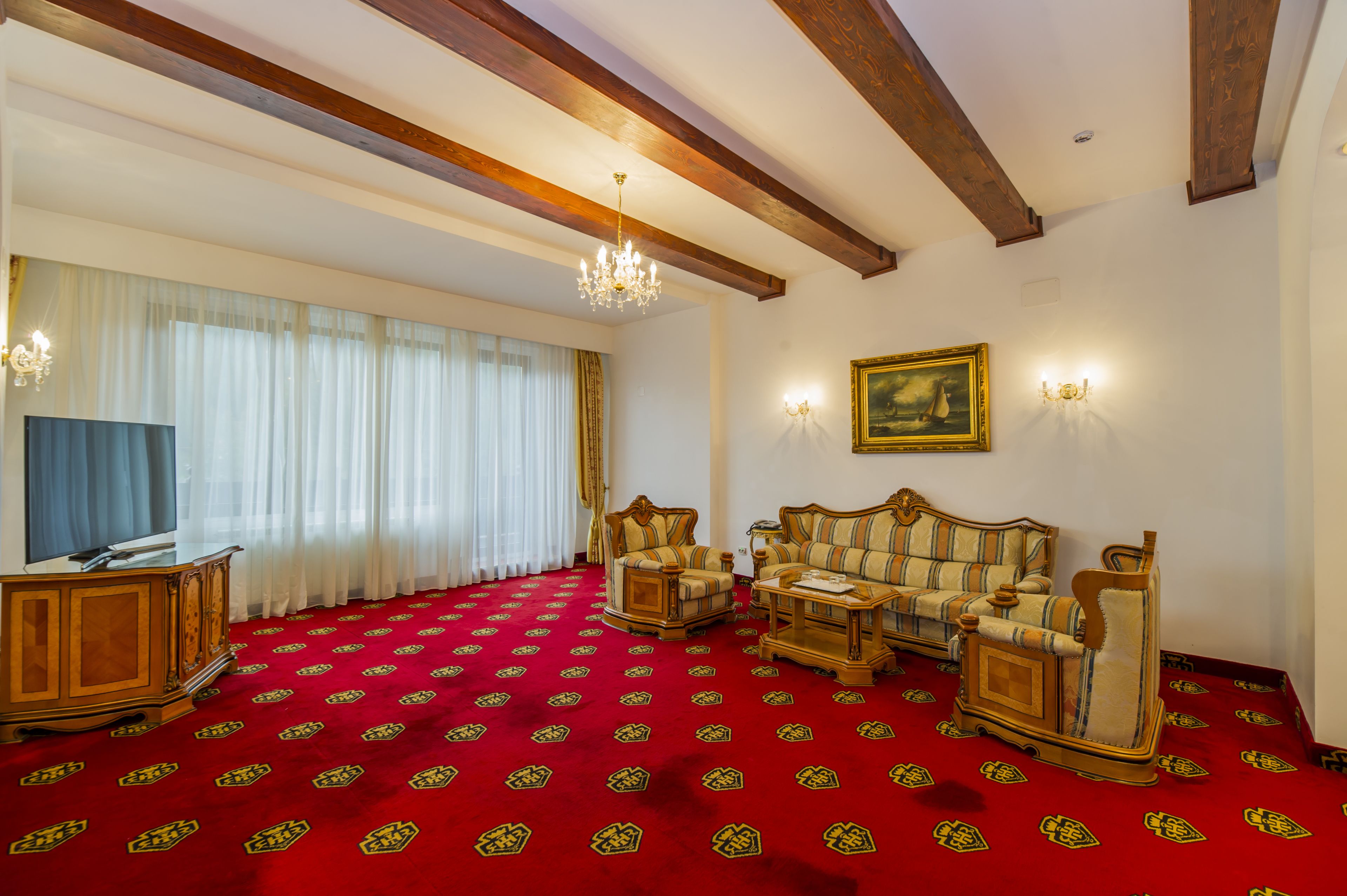 Ein Zimmer mit rotem Teppich, Holzmöbeln, einem Chandelier und einem Gemälde an der Wand.