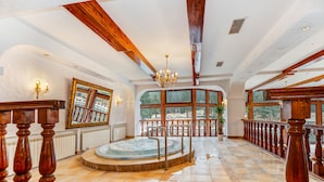 Amplio espacio interior con un jacuzzi grande, vigas de madera y vistas por ventanas amplias.