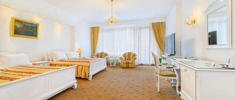 A hotel room with two beds, a desk, a chair, a TV, and a chandelier.