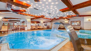 Una amplia piscina interior con caída de agua, vigas de madera y varias zonas de estar.