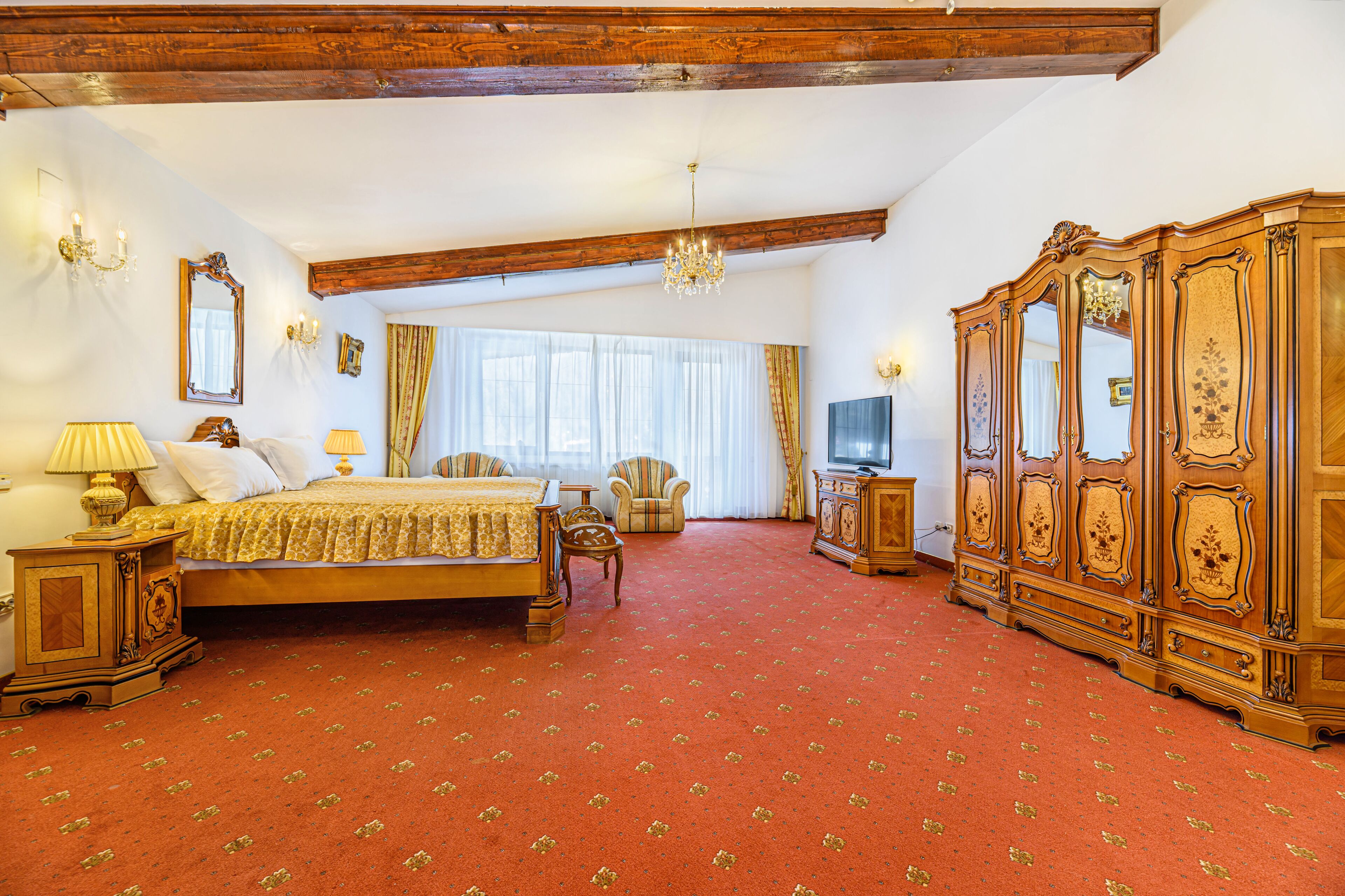 Une chambre spacieuse avec un grand lit, une armoire en bois, une télévision et un lustre.