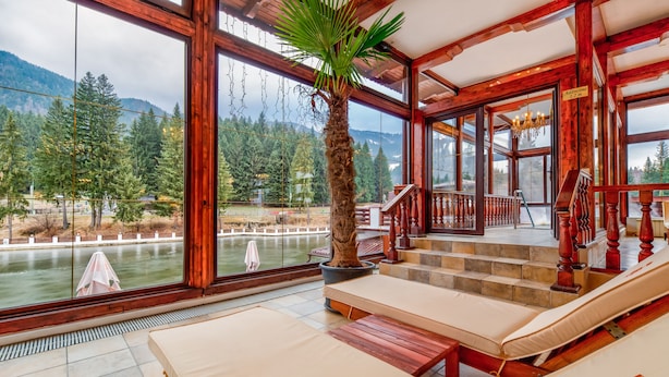 Habitación con amplia ventana que da a un lago y bosque, muebles de madera y una escalera que sube a un nivel superior.