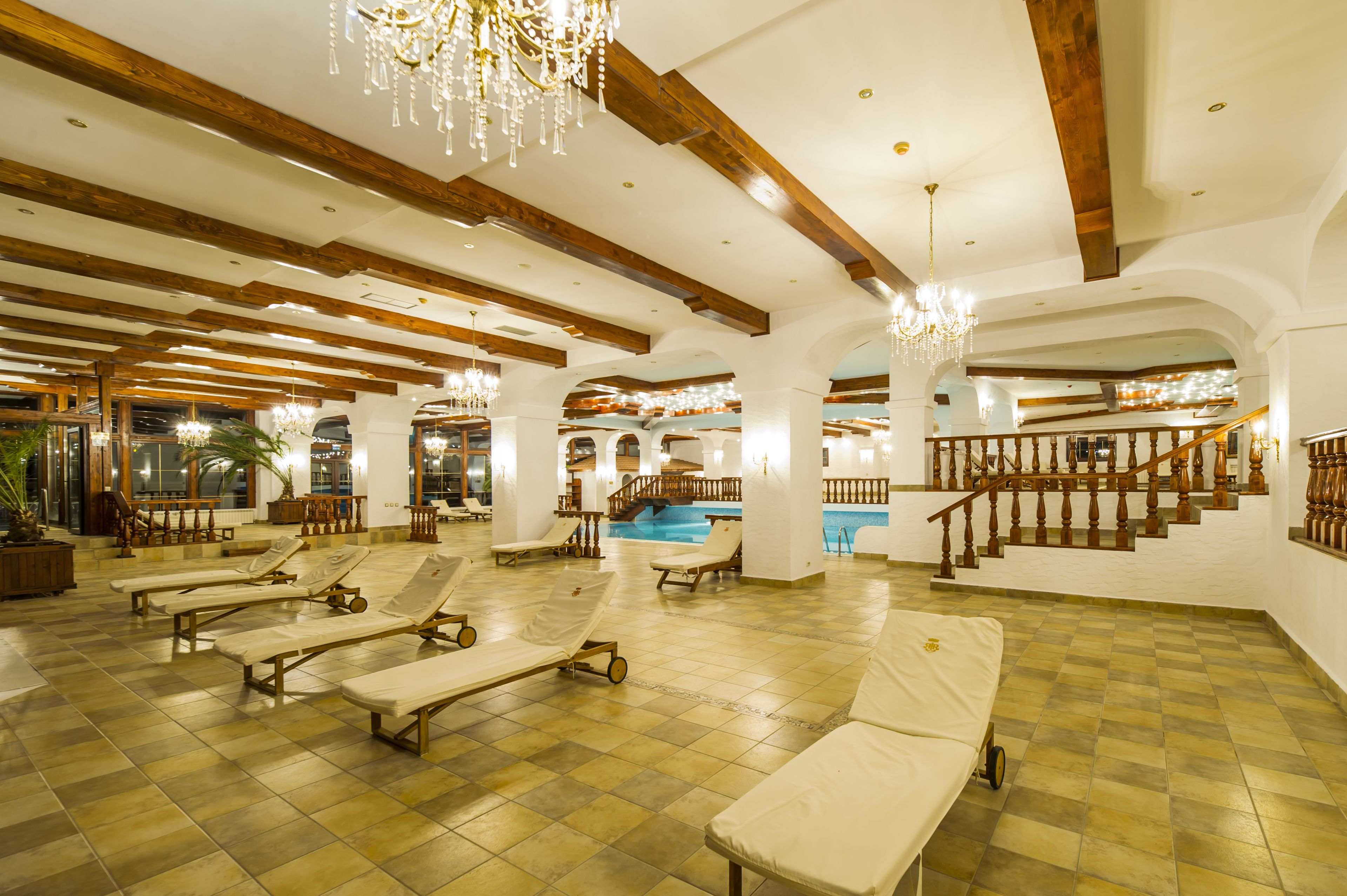 A spacious indoor area with sun loungers, a pool, wooden beams, and a staircase.