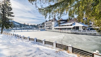 A riverside hotel with a snow-covered landscape, a wooden fence, and a view of the river.