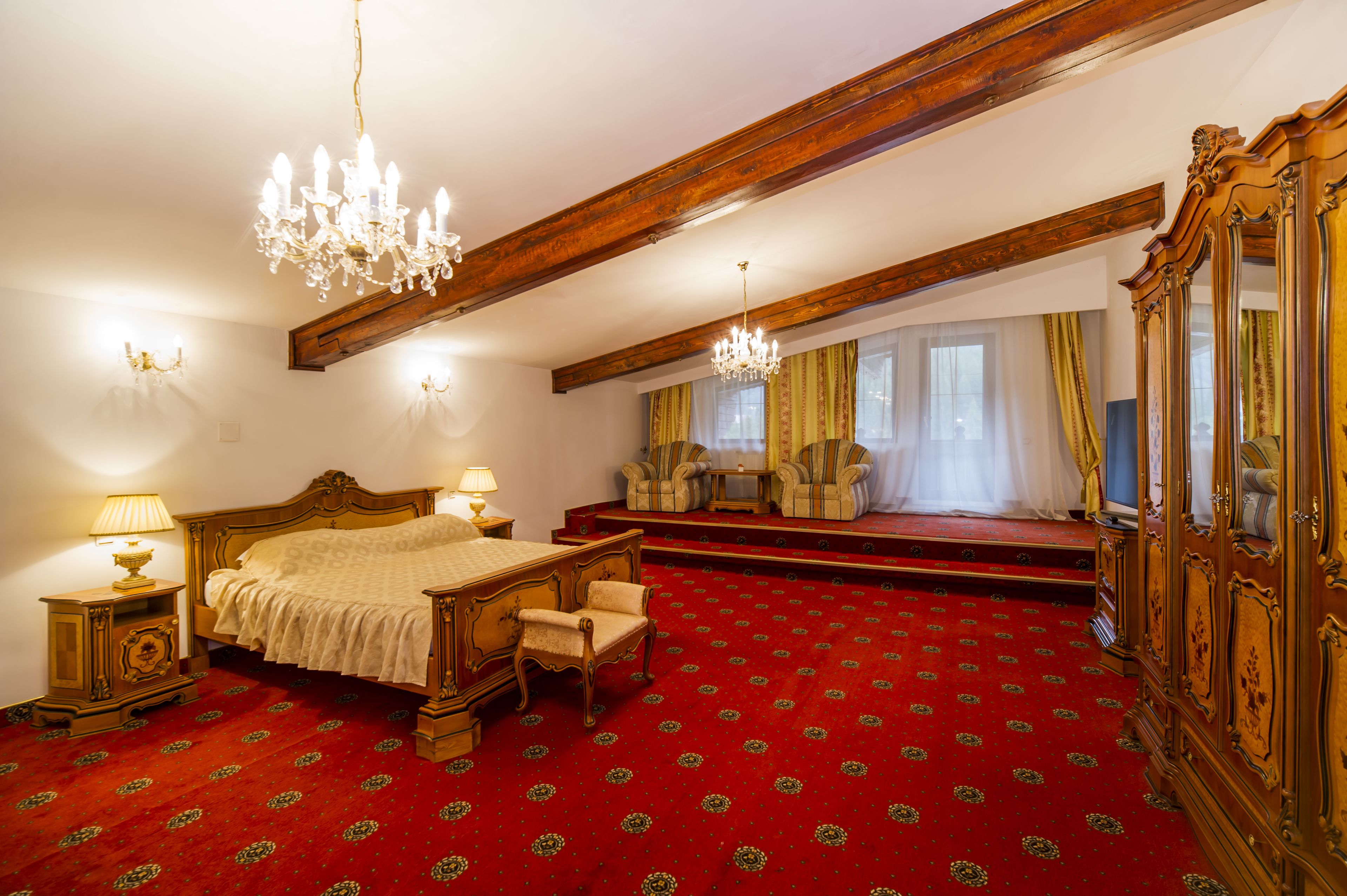 A bedroom with a large bed, two chairs, a wooden wardrobe, and a red carpet.
