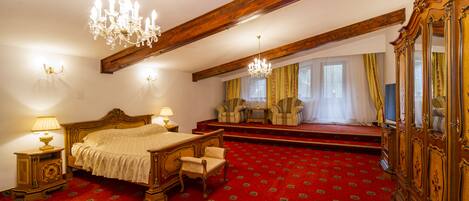 A bedroom with a large bed, two chairs, a wooden wardrobe, and a red carpet.