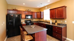 A kitchen with wooden cabinets, a black refrigerator, a microwave, a stove, and a sink. - 4 bedroom house close to the Horse Park (Georgetown)